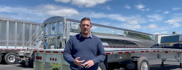Man stands in front of flatbed trailer.